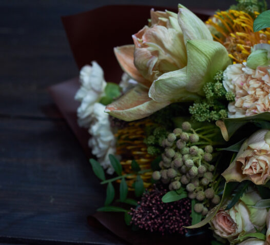 Bukett med olika blommor, inklusive rosor och gröna blad, på ett mörkt underlag.